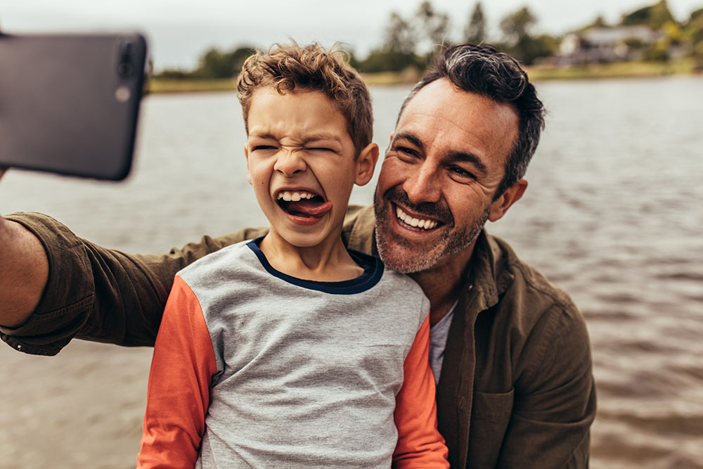 father son taking selfie by the water